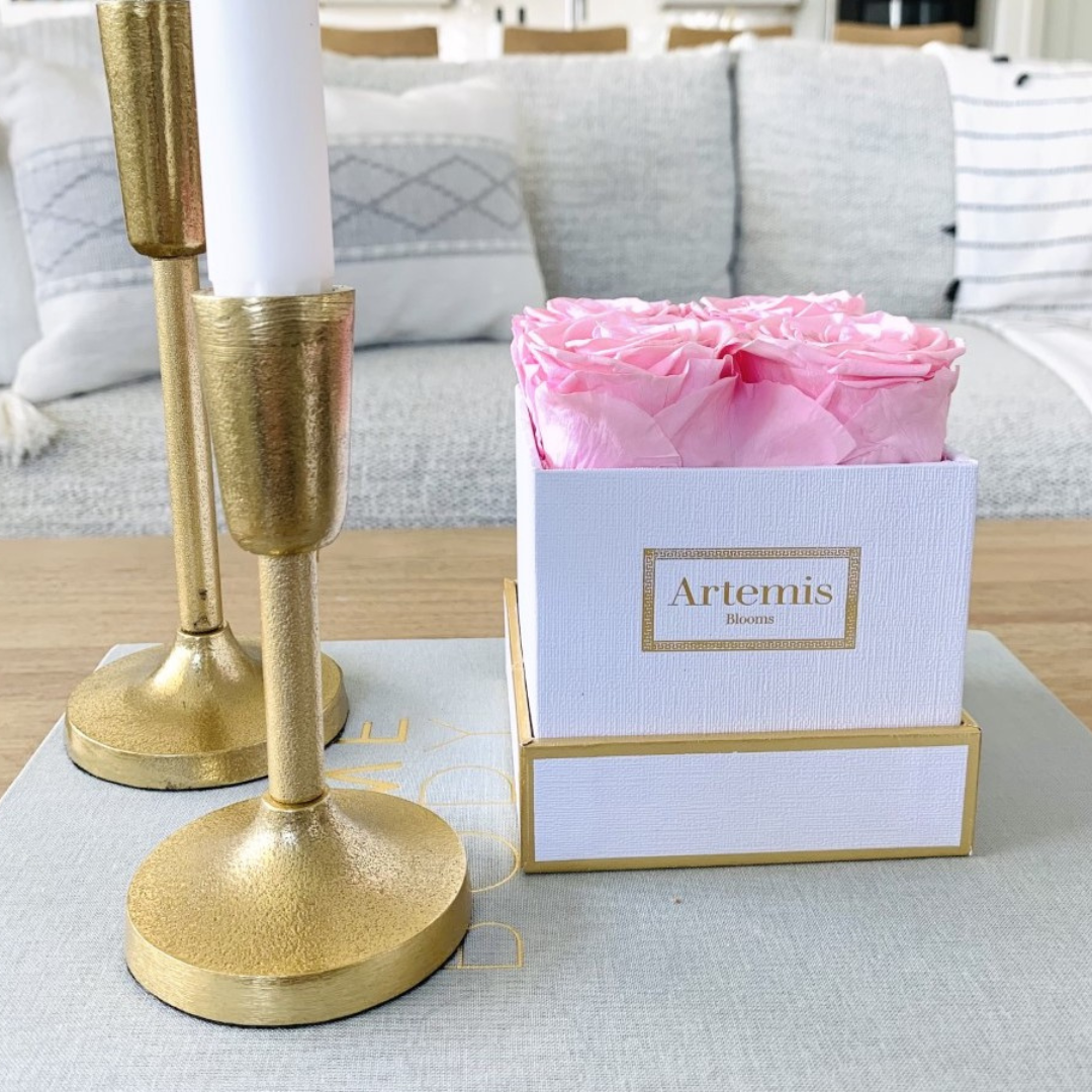 Light pink roses in a white box with two gold candlesticks on a coffee table
