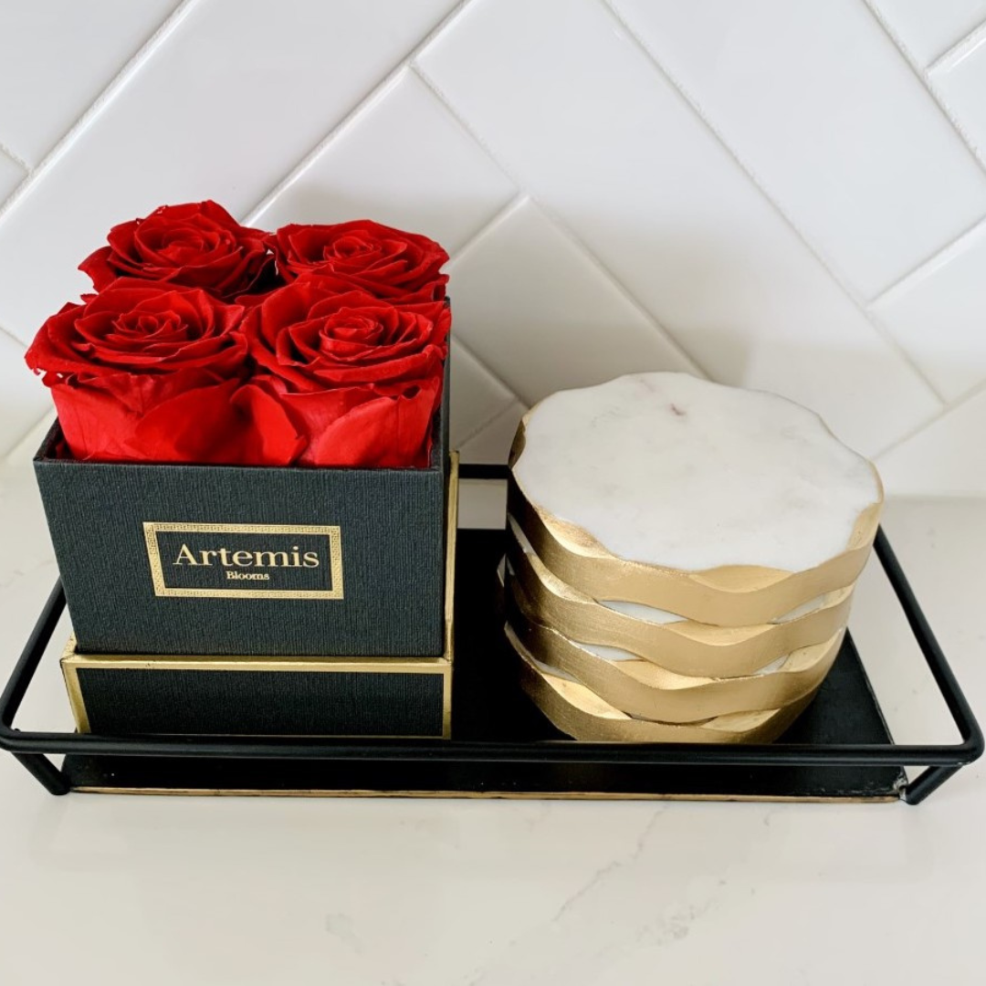 Red roses in a black box next to marble coasters in a black metal tray