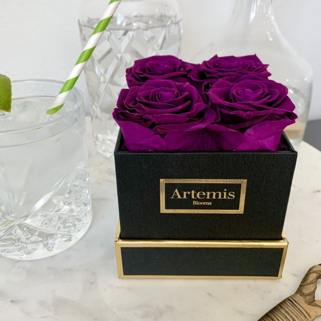 Dark purple roses in a black box next to a mixed drink on a bar cart